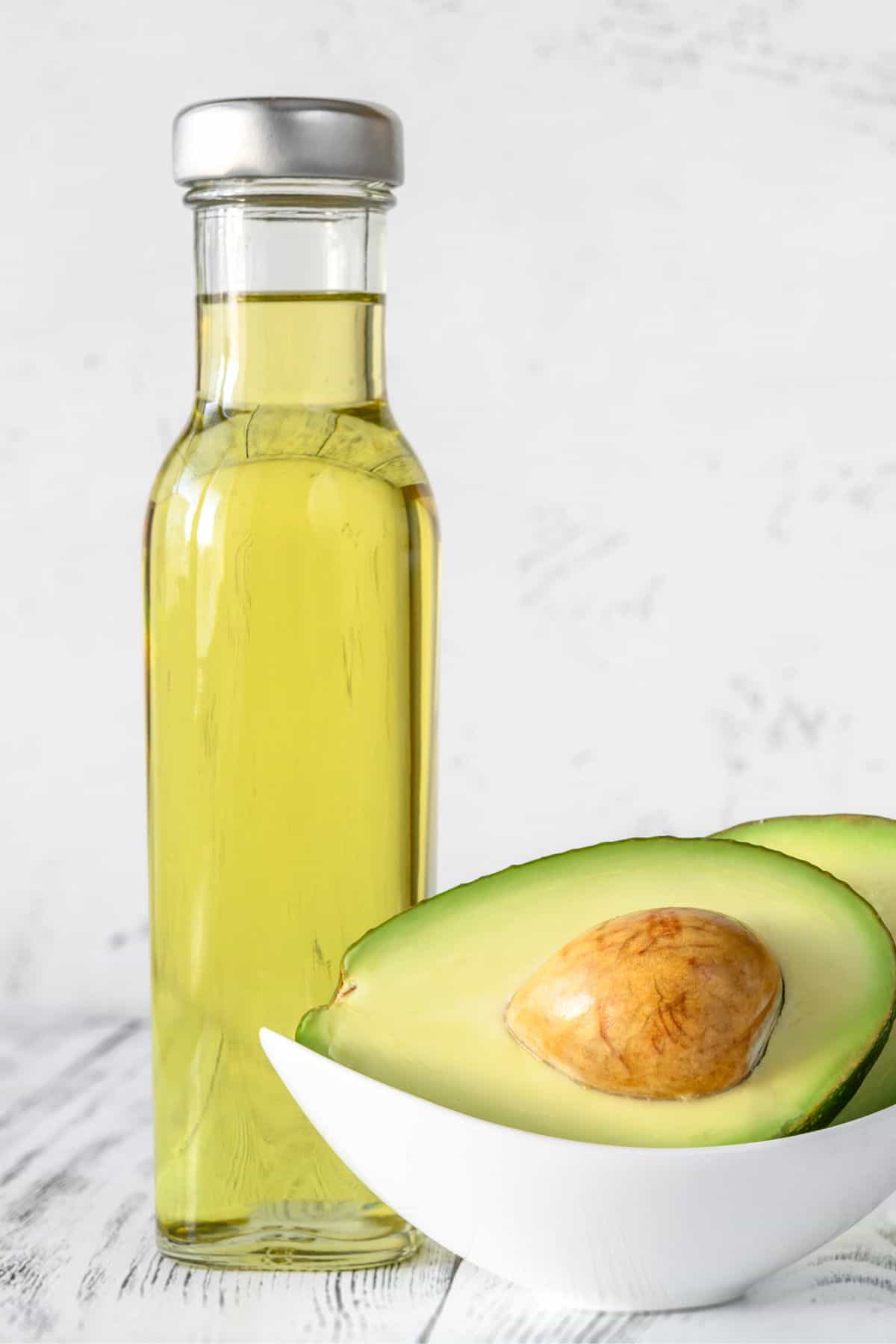 bottle of avocado oil with raw avocado next to it in a dish.